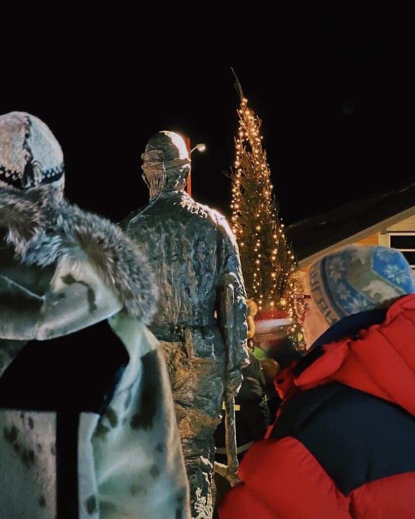 Locals in warm clothes by the lit Christmas tree and the miner statue in Longyearbyen